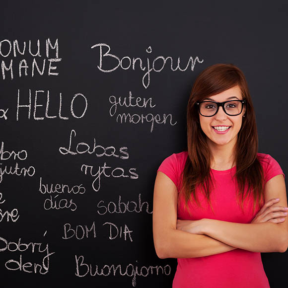 Language teacher beside a blackboard of greetings in different languages
